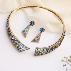 Gold open choker necklace with blue stone detailing and matching triangular earrings on white background