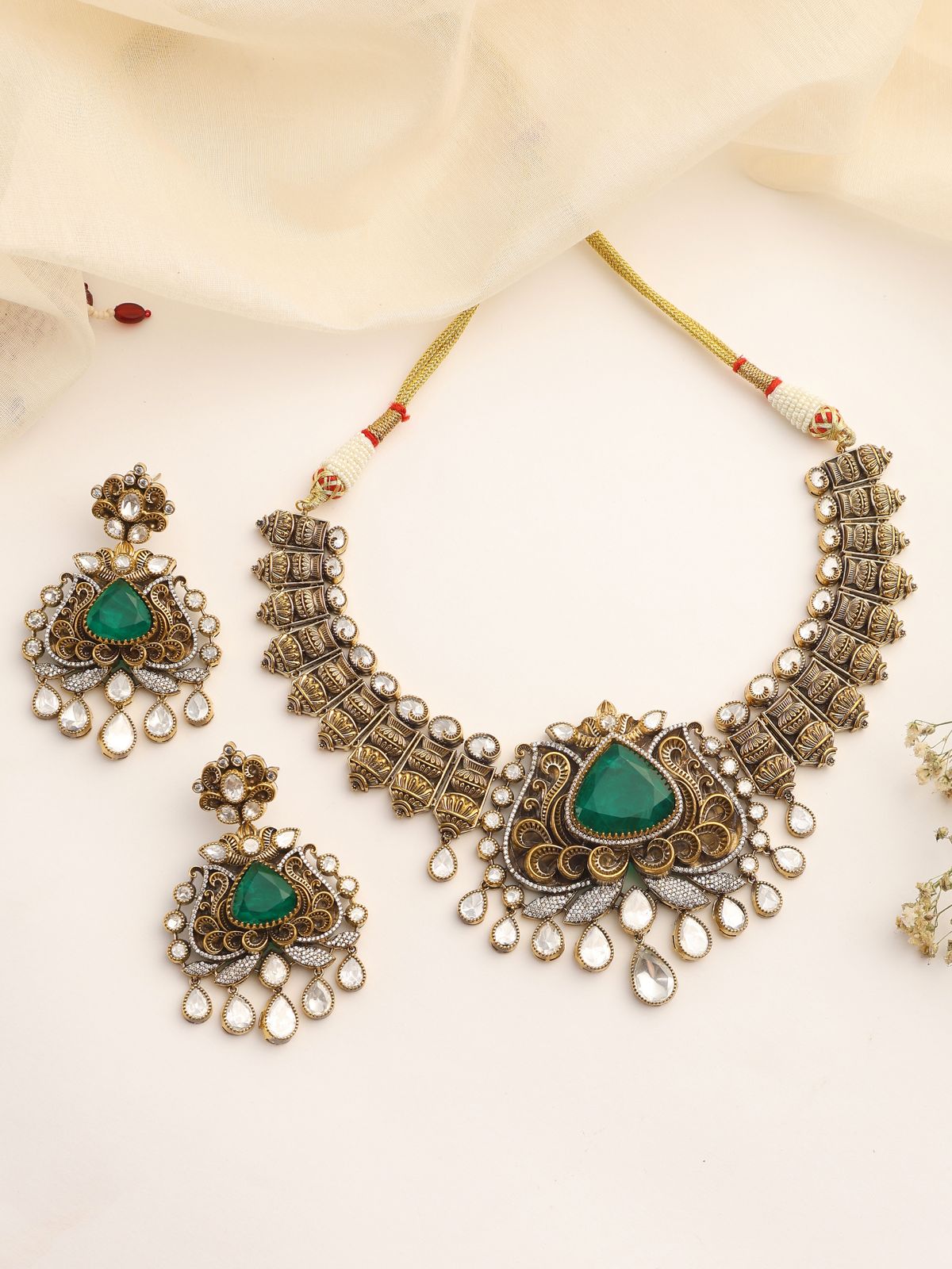 Ornate necklace with green stones and matching earrings on a light background