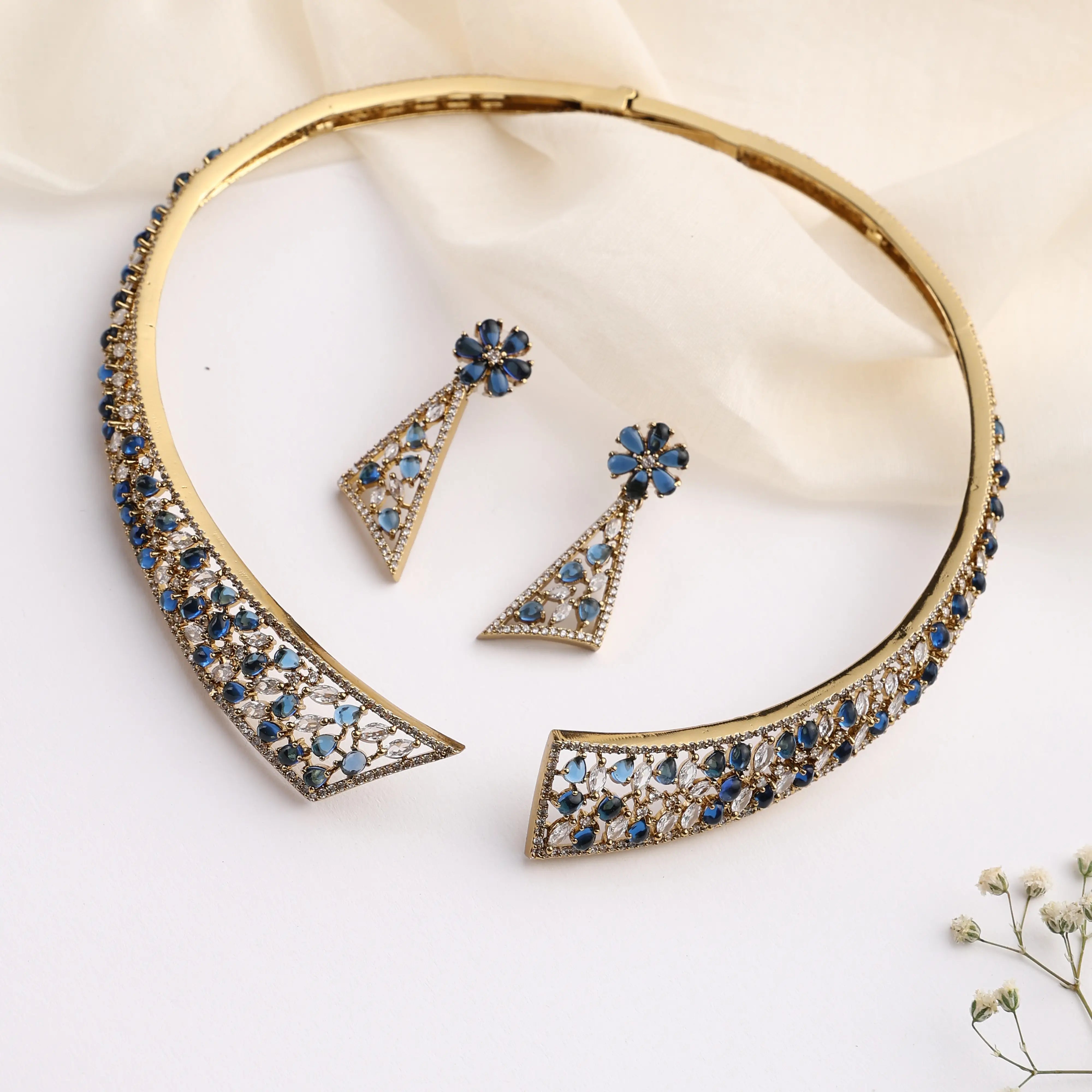 Gold open choker necklace with blue stone detailing and matching triangular earrings on white background