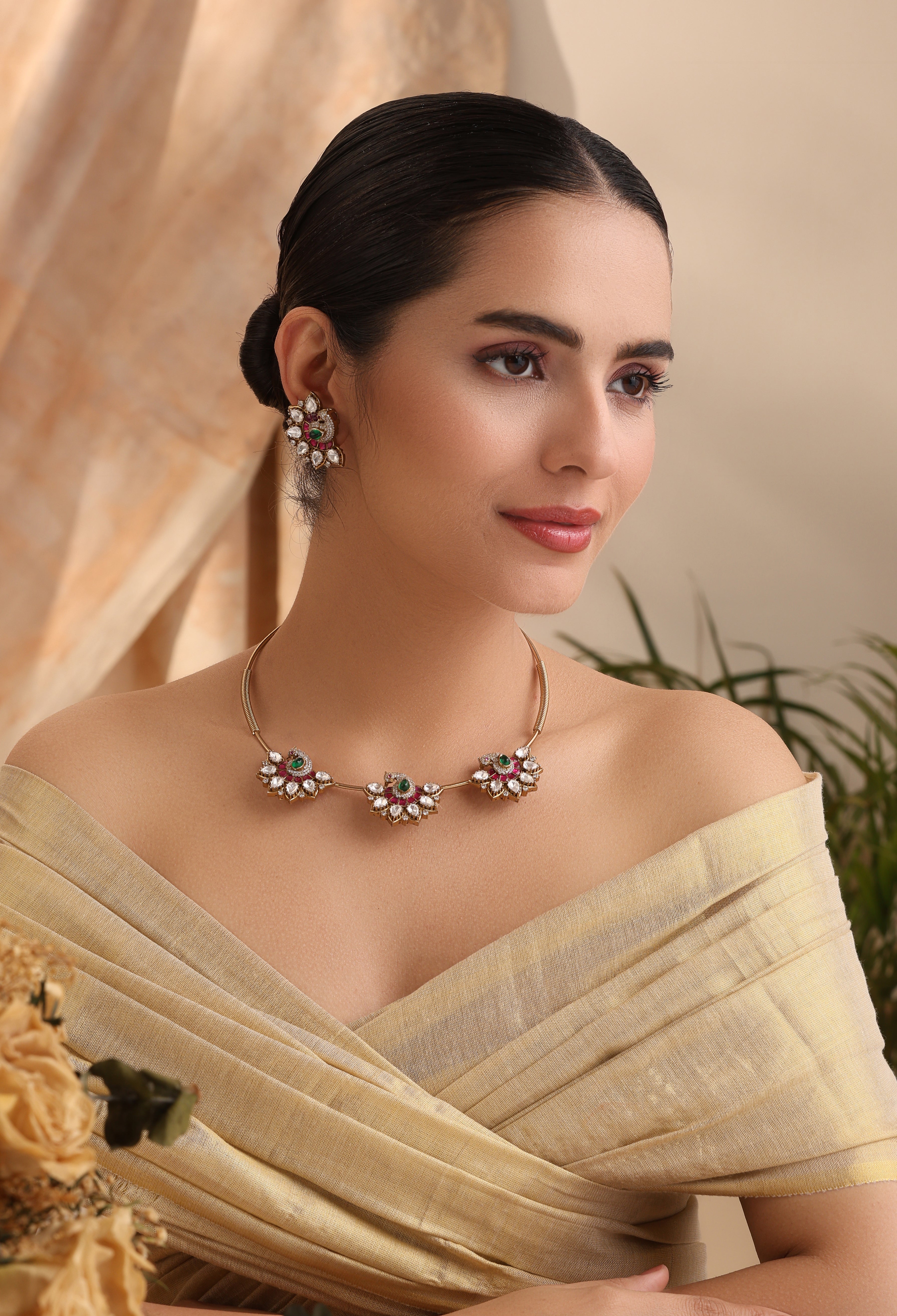 Model wearing Anaya Blossom Masonite Hasli Set – gold-tone choker with emerald & ruby floral motifs and matching stud earrings.