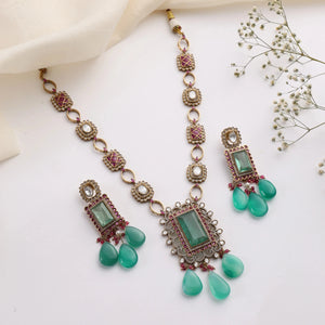 Flatlay of emerald ruby Kundan necklace set with rectangular pendant and matching drop earrings.