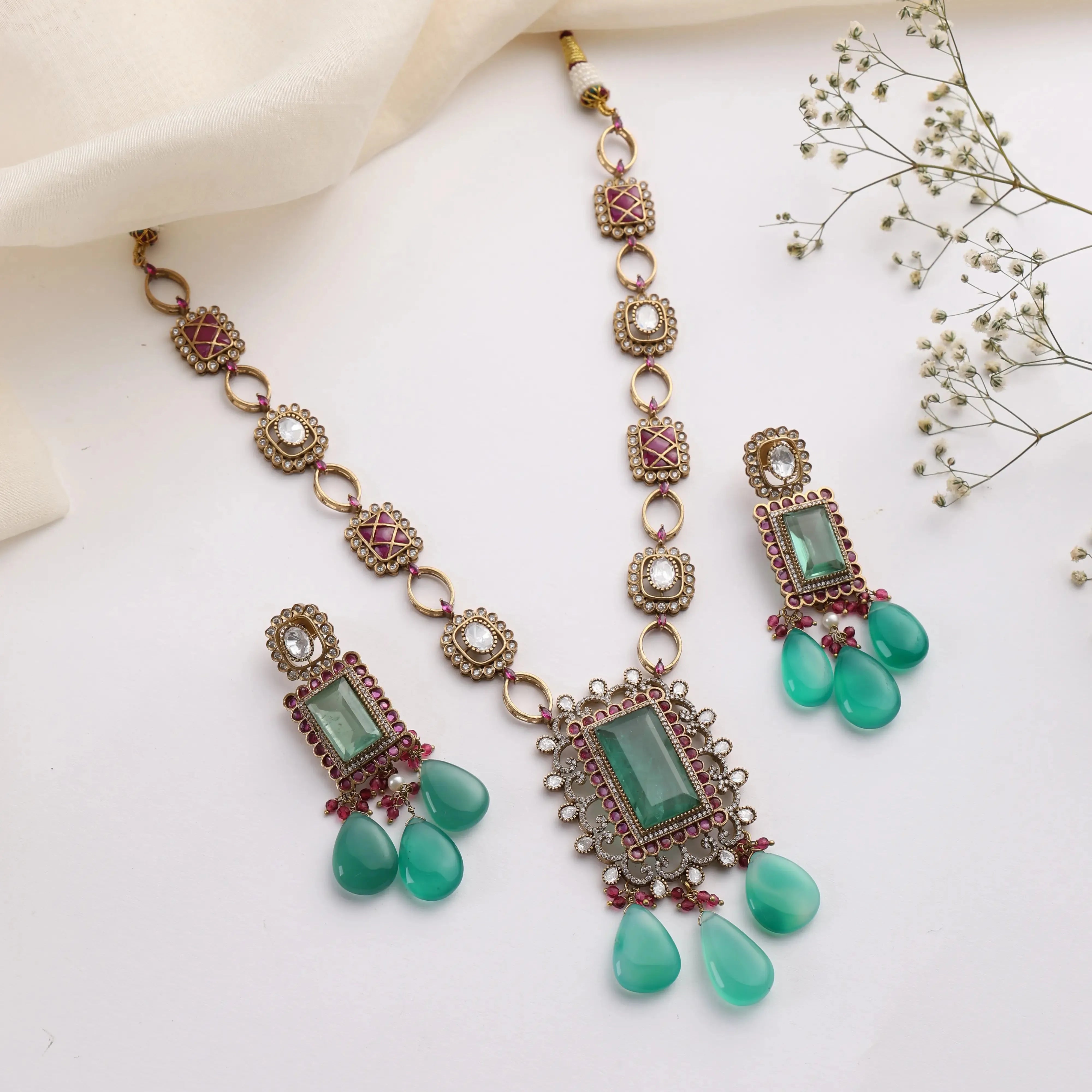 Flatlay of emerald ruby Kundan necklace set with rectangular pendant and matching drop earrings.