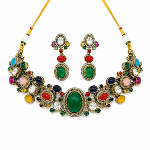 An ornate Indian style jewelry set featuring a statement necklace and matching drop earrings. The set is decorated with multiple colorful stones including green, red, blue, pink, yellow, and white, set in gold-toned metal with clear rhinestone accents.