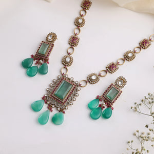 Close-up flatlay of emerald ruby Kundan necklace chain and earrings with green teardrop beads.