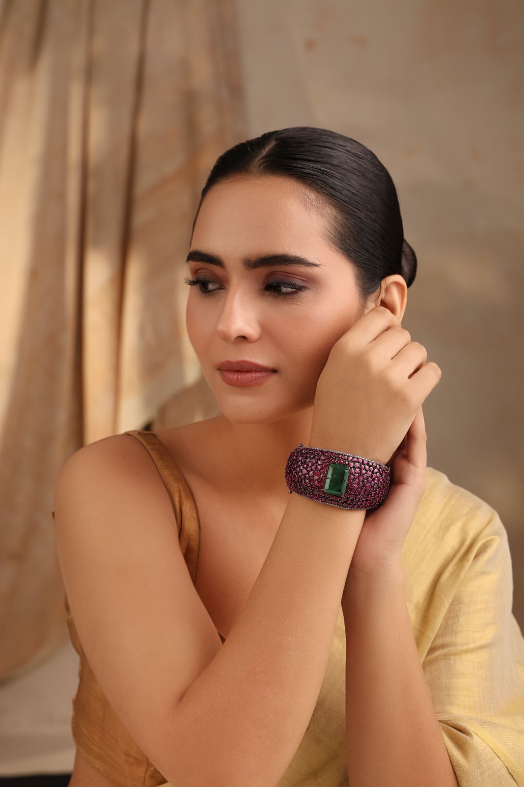 Model wearing wide cuff bracelet with emerald green centerpiece and ruby pink stones