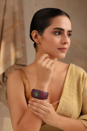 Model wearing wide cuff bracelet with emerald green centerpiece and ruby pink stones